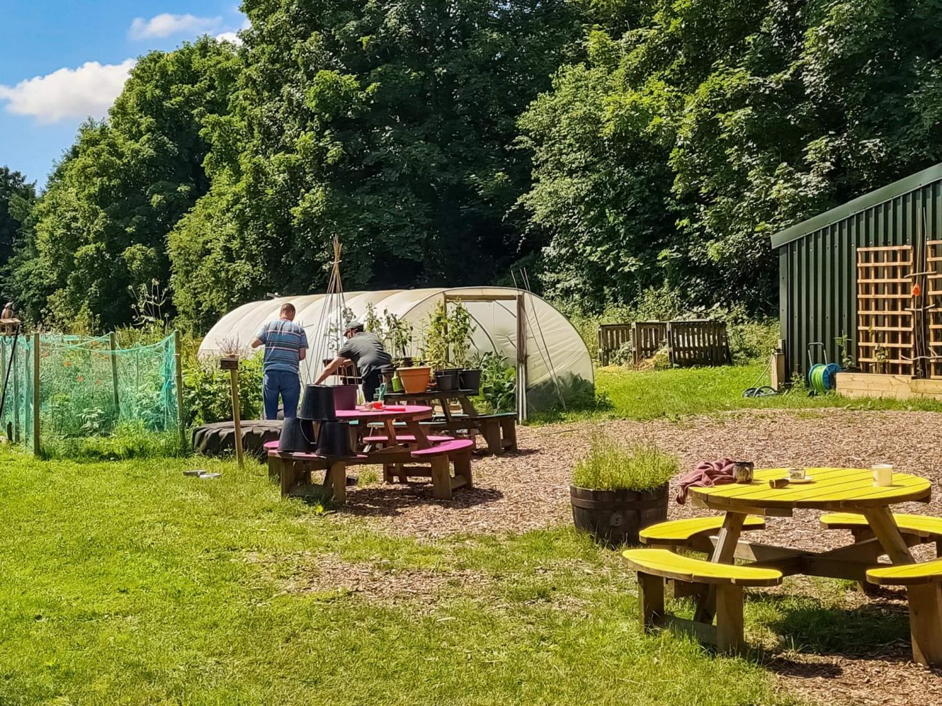 Two adults working outside near a greenhouse.