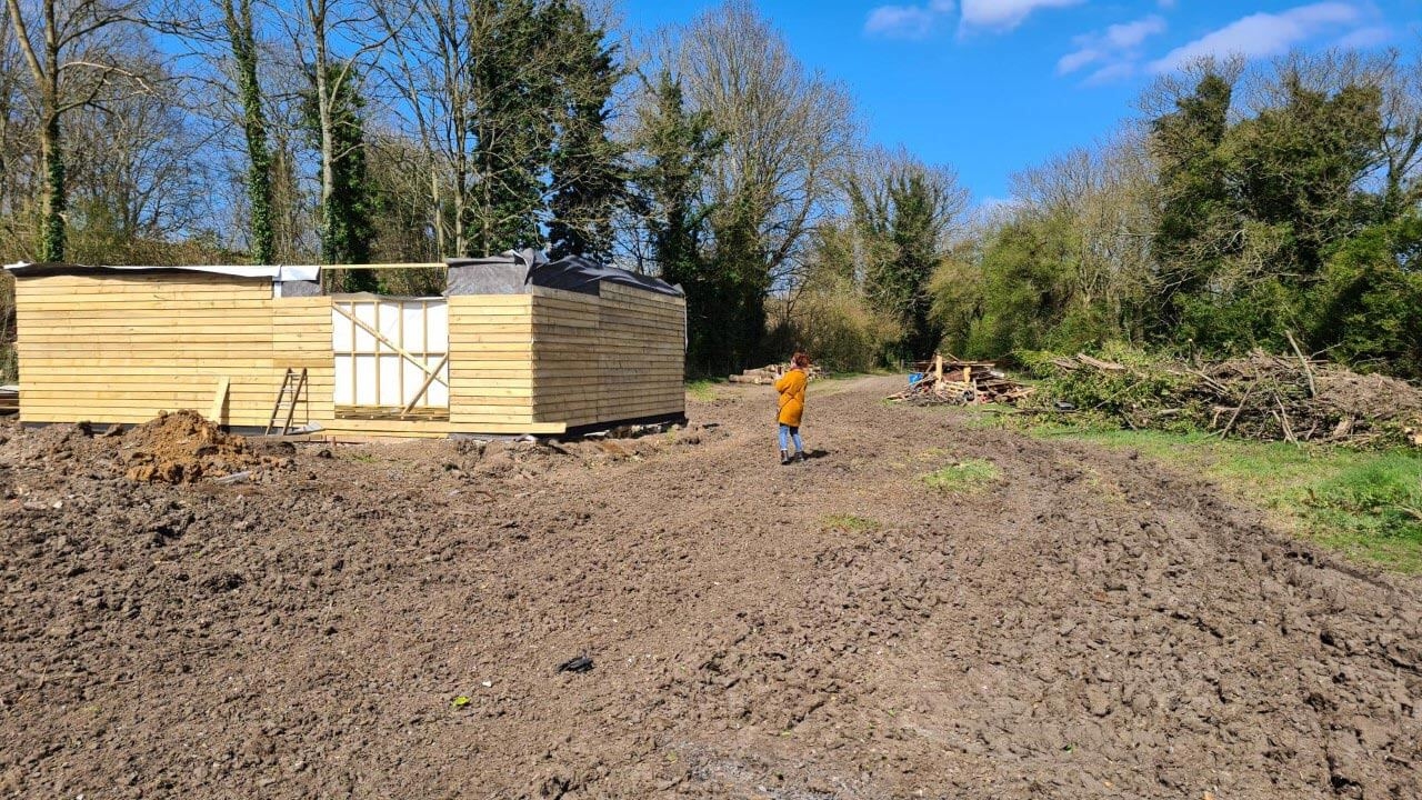 Wooden building midway through construction on a muddy field.